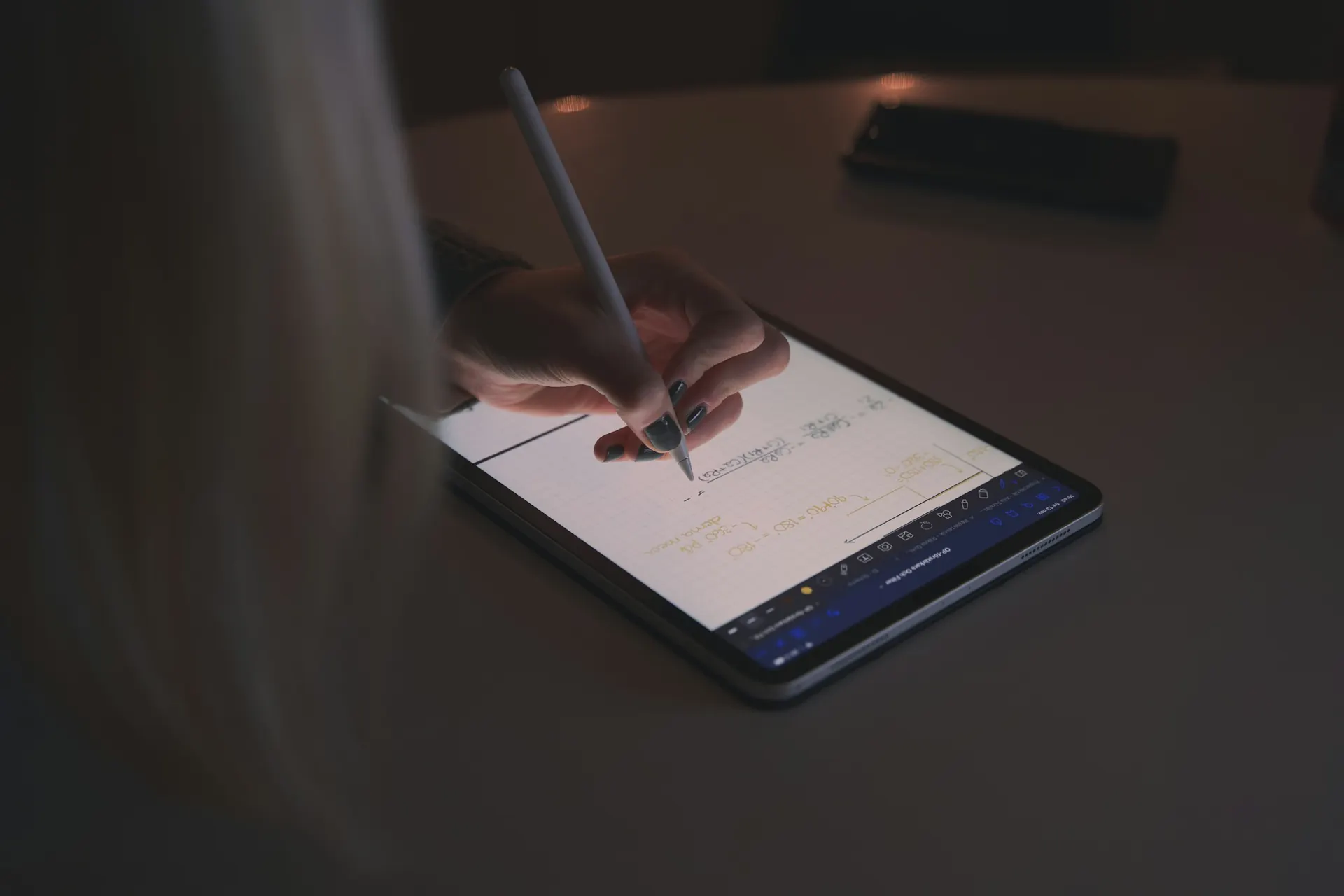 يد تحل مسائل على جهاز لوحي بالقلم الرقمي في إضاءة خافتة